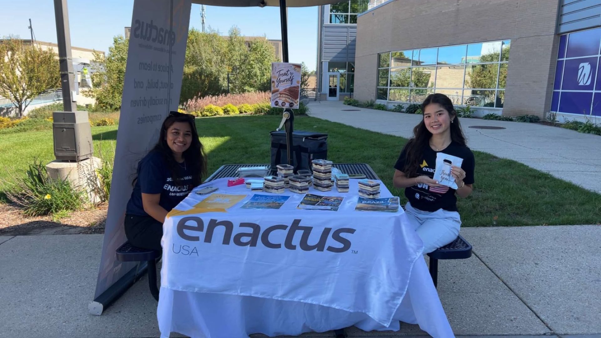 Two members at an Enactus table on campus, selling treats to fund the World Cup trip