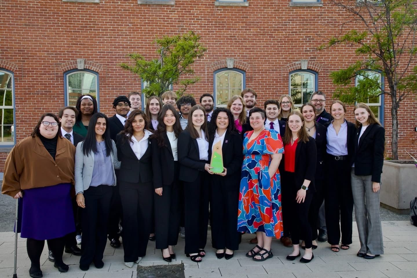 The UWW Enactus team with the national championship trophy outside a brick building